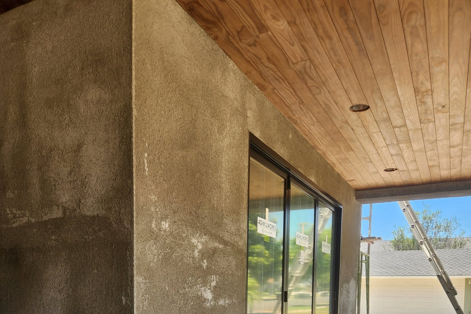 A stucco wall under a boxed timber soffit, beside a sliding door