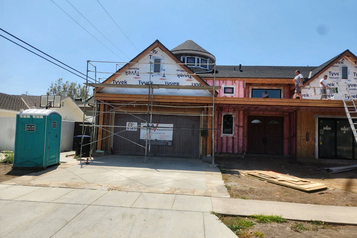 The same house stripped to sheathing and weather wrap, scaffolded, with the second story framed and crew on the roof