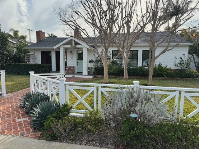 The house from the street behind its ranch fence, brick path and mature planting