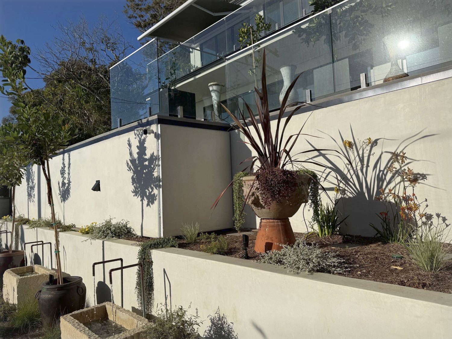A stucco retaining wall with a glass rail above it and planting built in