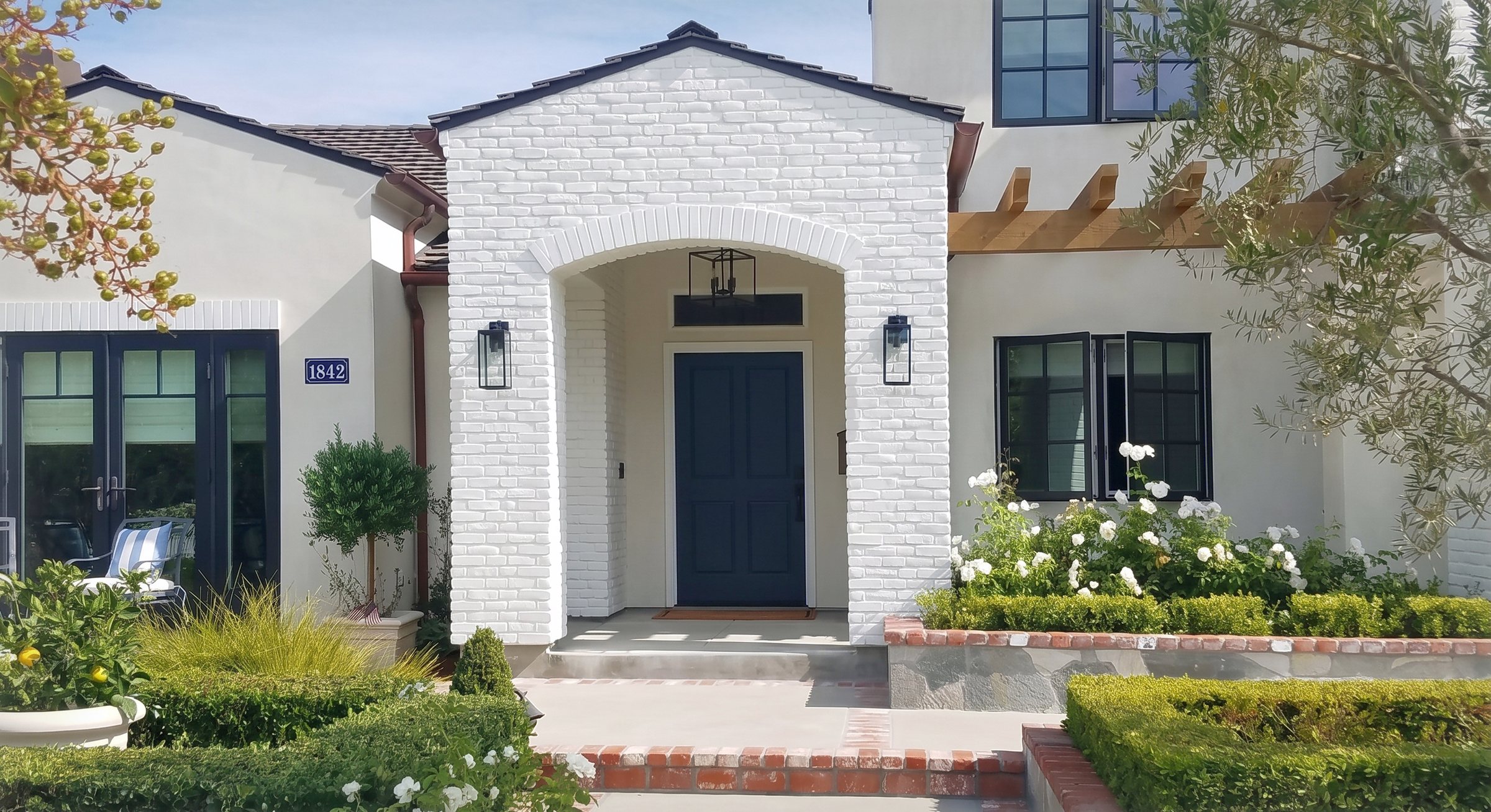 The rebuilt front elevation in white brick, the arched entry and its navy door under exposed rafter tails
