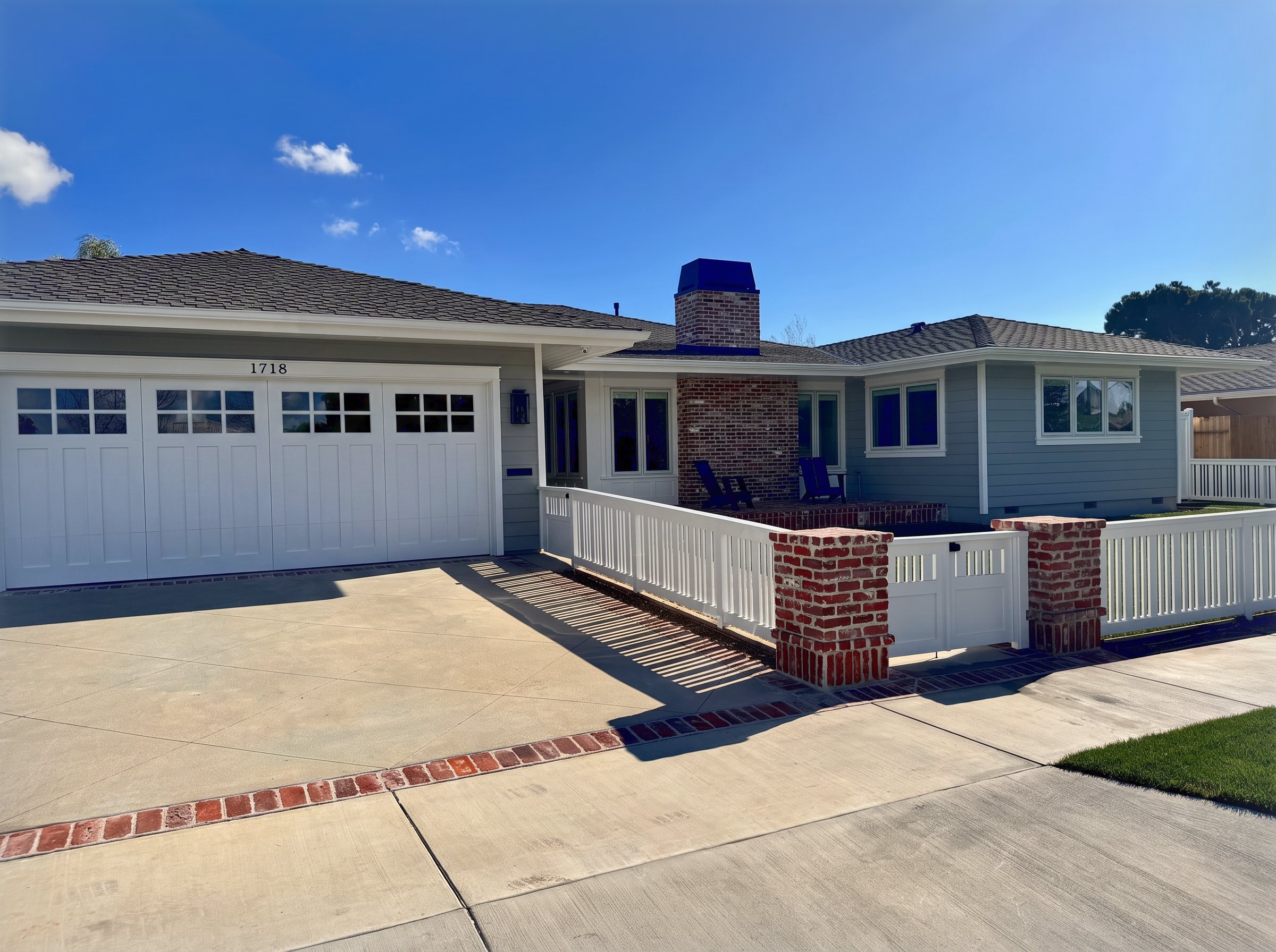 The house from the driveway, brick chimney and brick planters against blue gray siding