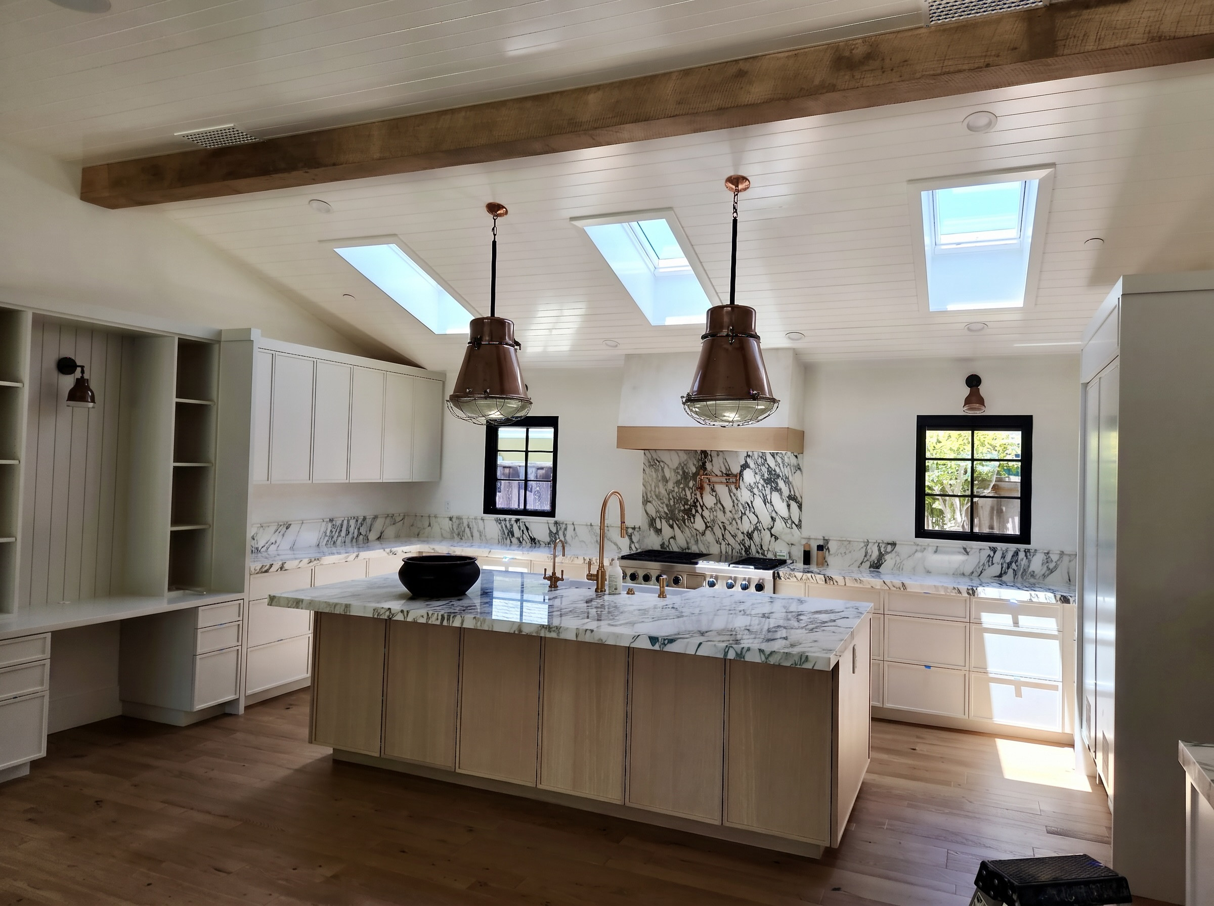 A Newport Beach kitchen under skylights, copper pendants over a marble island