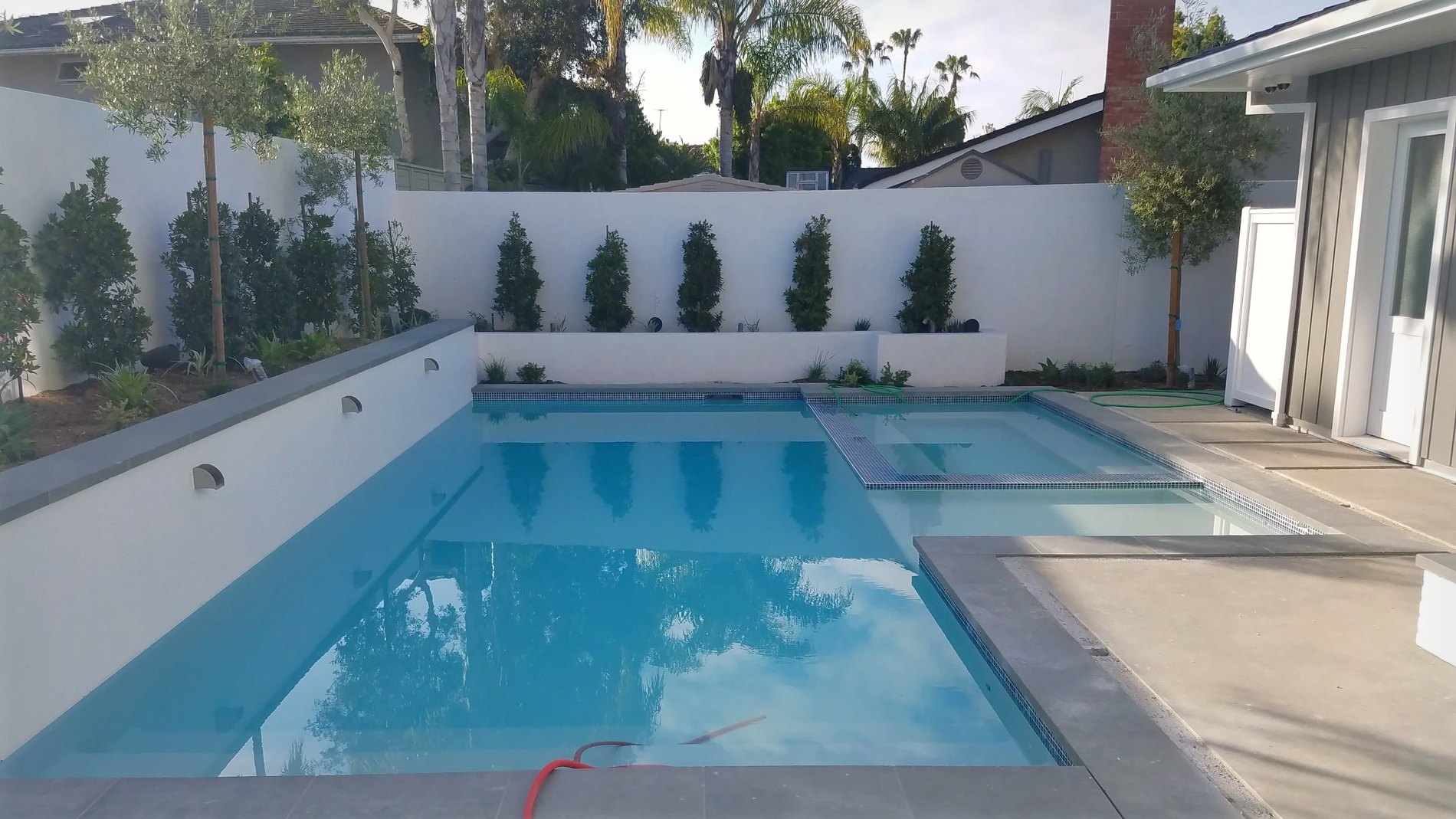 The pool and spa against the rendered garden wall, scuppers and cypress behind