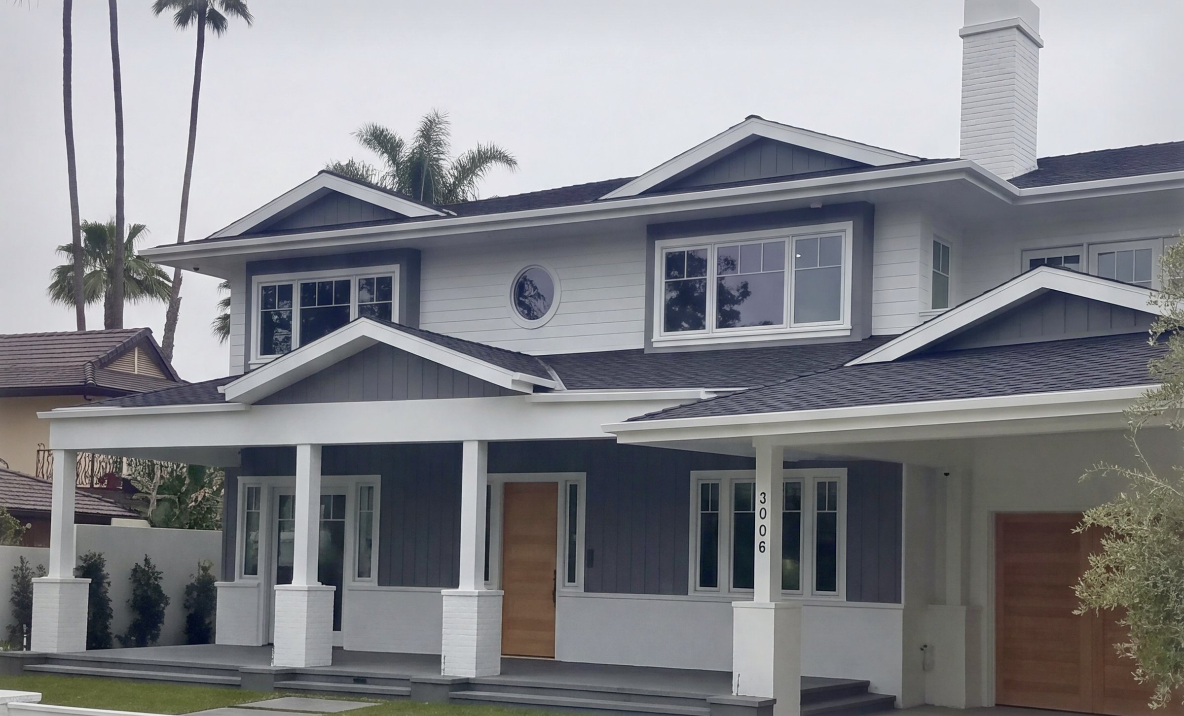 Two stories in lap siding and board and batten, the deep porch on square columns with the porthole window above