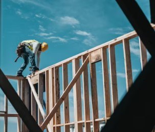 A carpenter working on the stud framing of the new upper floor against an open sky.