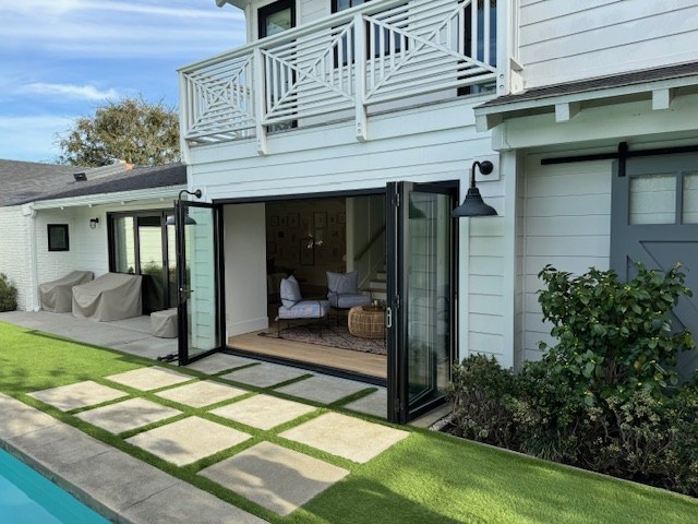 The rear elevation with the bi-fold doors folded open to the lawn, the pool and the stone pavers.
