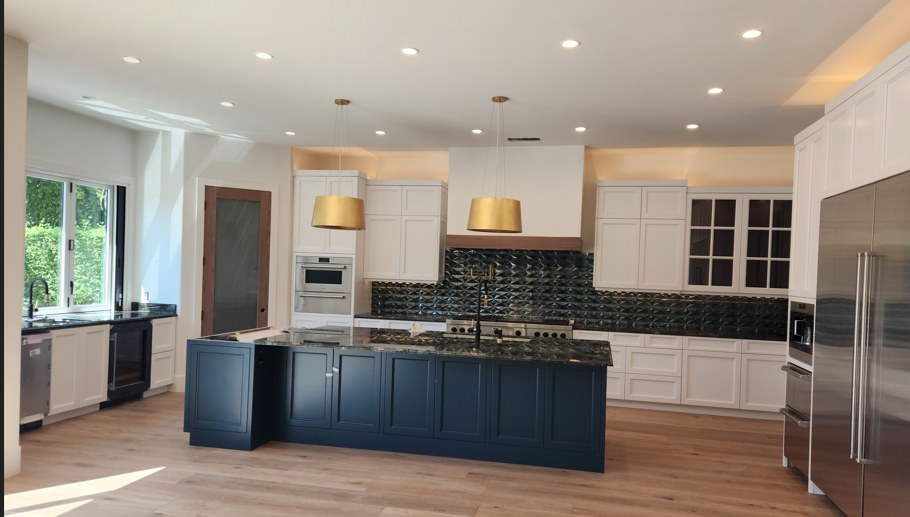 The kitchen, a navy island under brass pendants against white cabinetry and a dark tile backsplash.