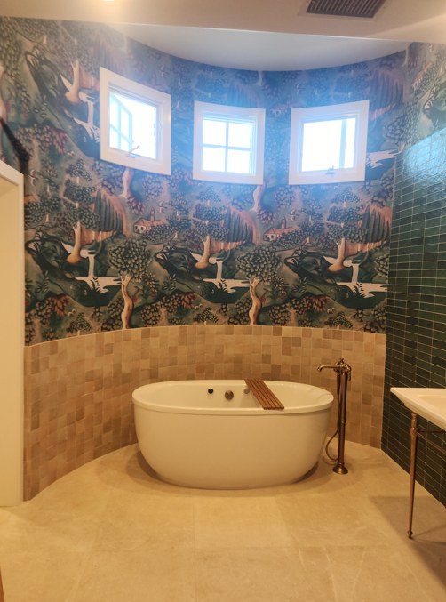 The primary bathroom, a freestanding tub below clerestory windows against a botanical mural.