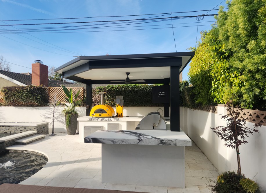 The outdoor kitchen under its black pavilion, a marble waterfall counter and built-in grill at the pool edge.