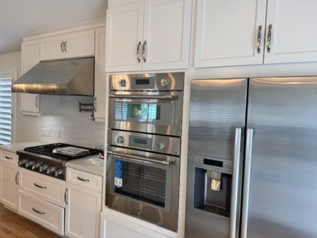 The original kitchen, wall ovens and a gas range in white cabinetry, before the remodel.