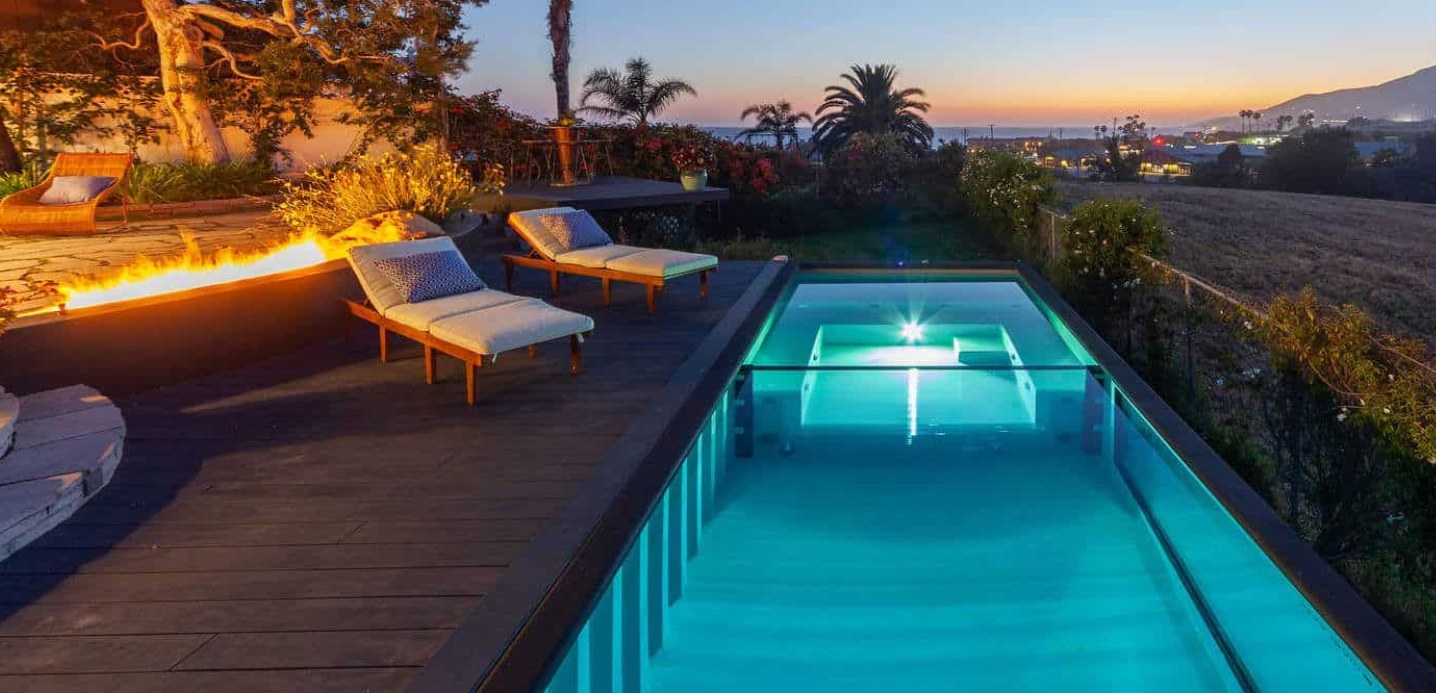 The Modpool container pool lit at dusk beside the fire feature, with the view out over the coast.