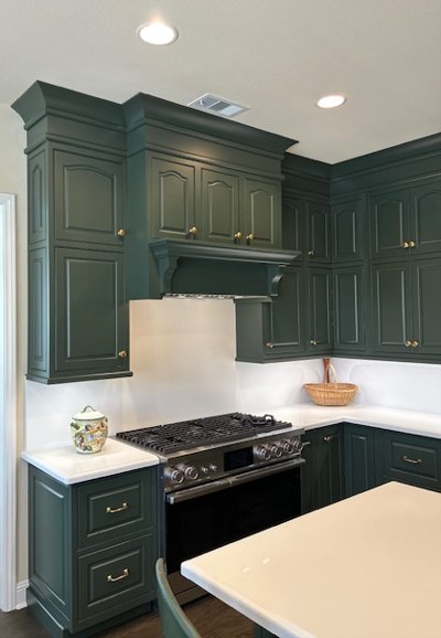 The range under its tall paneled hood, framed by green cabinetry.