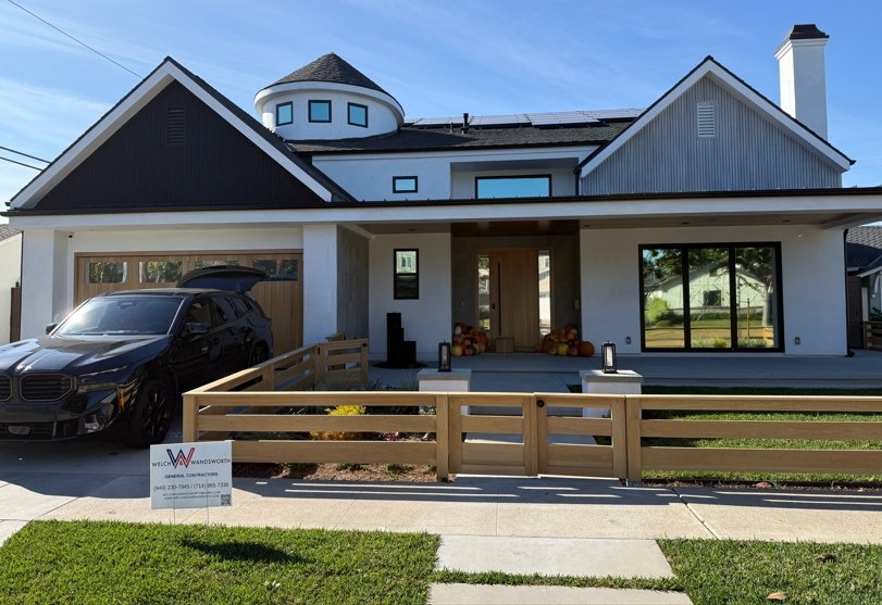 The completed front elevation, board and batten gables either side of a turret, behind a new post and rail fence.
