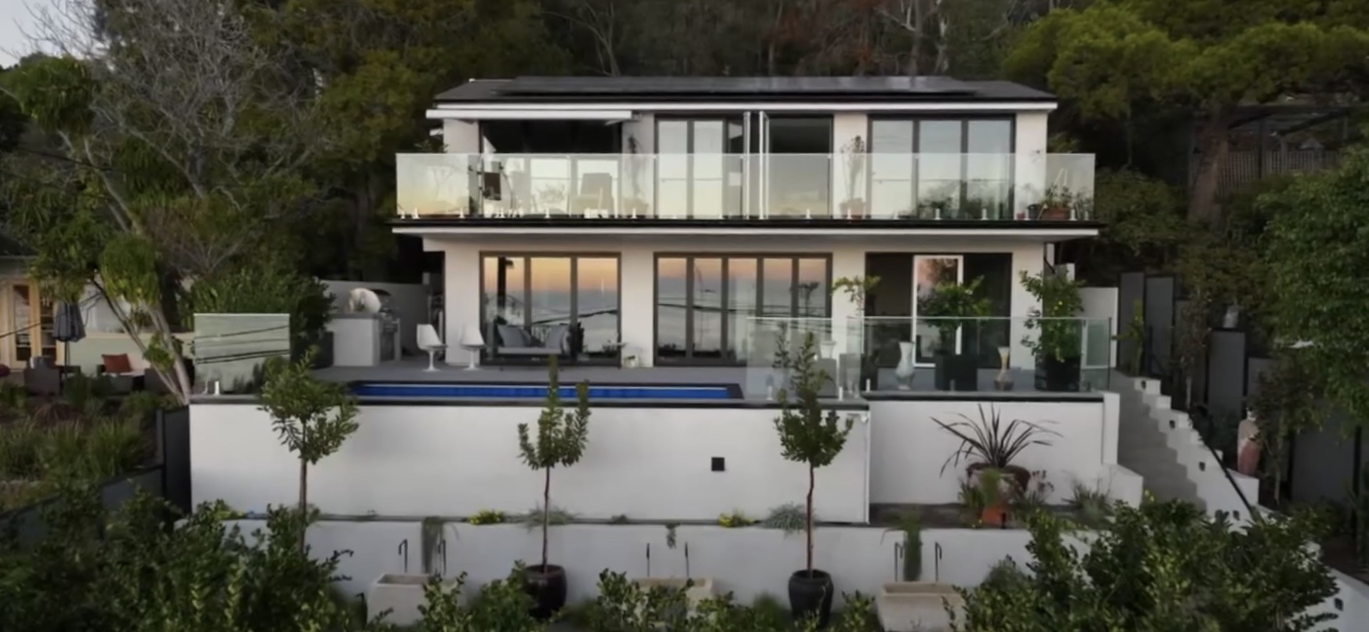 The finished Laguna Beach house at dusk, two levels of glass above the lap pool, with the ocean showing through the living room