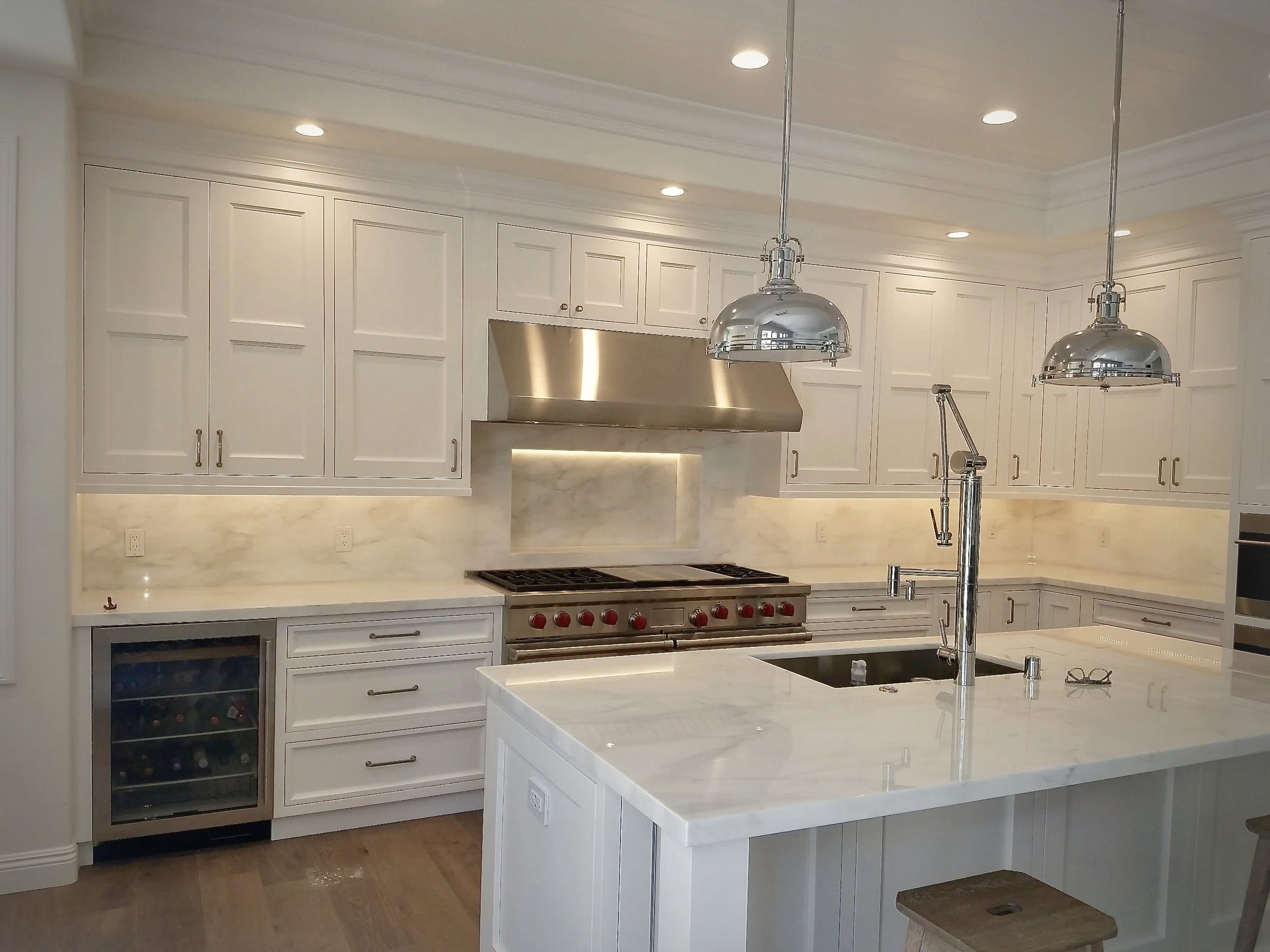 The new kitchen from the living side, marble island and waterfall end under polished nickel pendants